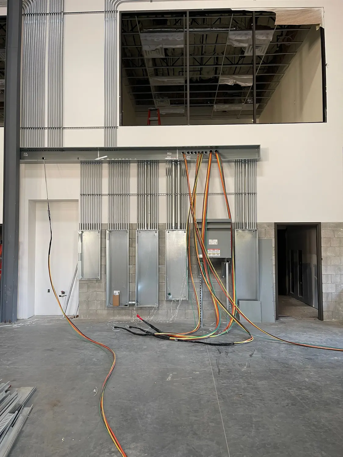 Electrical rough-in in a Bakersfield commercial build-out: parallel conduit runs feeding a row of new panelboards, with feeder conductors pulled to the gear and the ceiling still open.