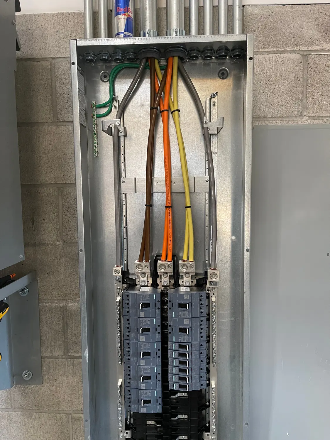 Feeder conductors dressed into the main lugs of a new commercial panelboard, with the branch breakers landed below and conduit stubbed into the top.