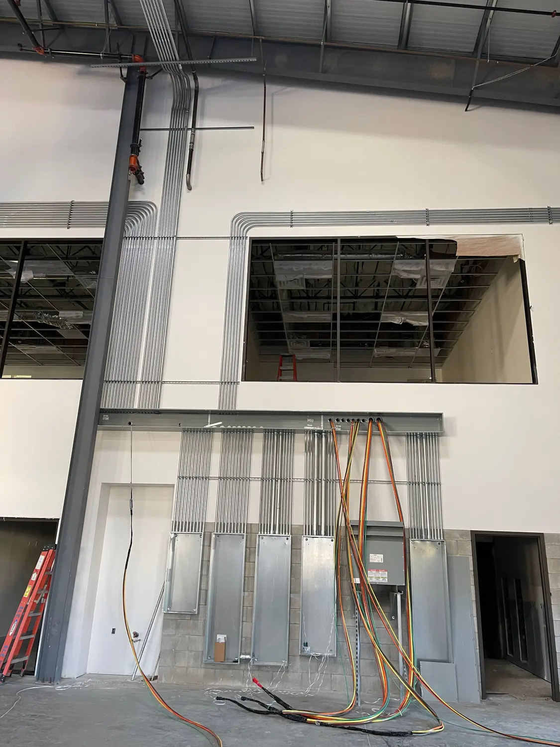 Electrical rough-in underway in a new commercial building in Kern County — conduit runs stubbed down to a row of panels, feeders pulled across the slab.