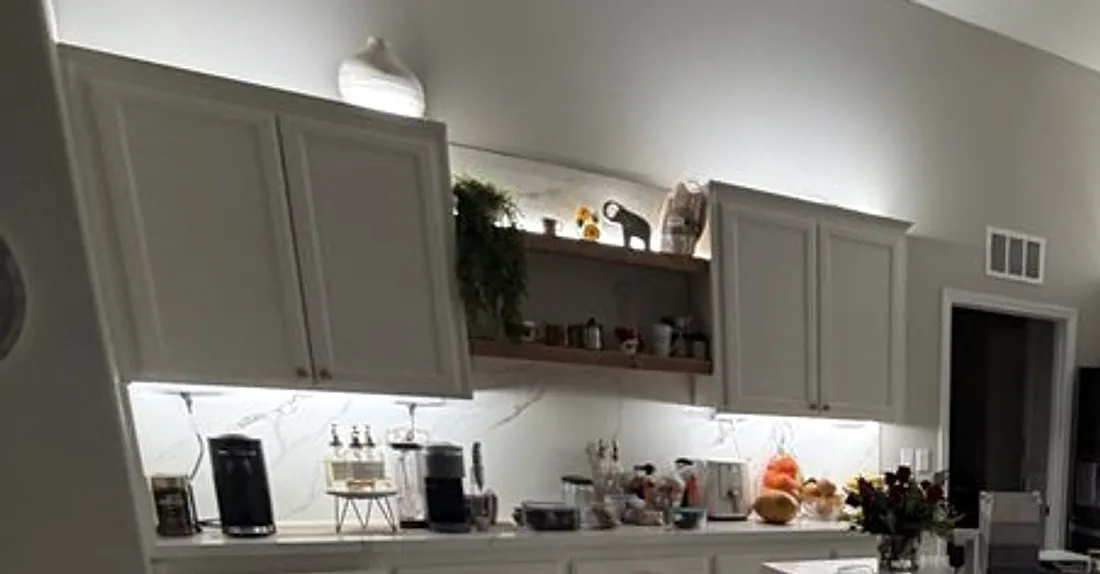 Layered lighting in a Bakersfield kitchen — under-cabinet LEDs washing the backsplash, a lit open shelf, and cove lighting above the cabinets.
